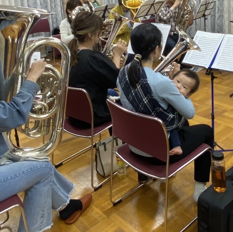 抱っこ紐の赤ちゃんが金管バンドの練習中に顔をのぞかせる様子
